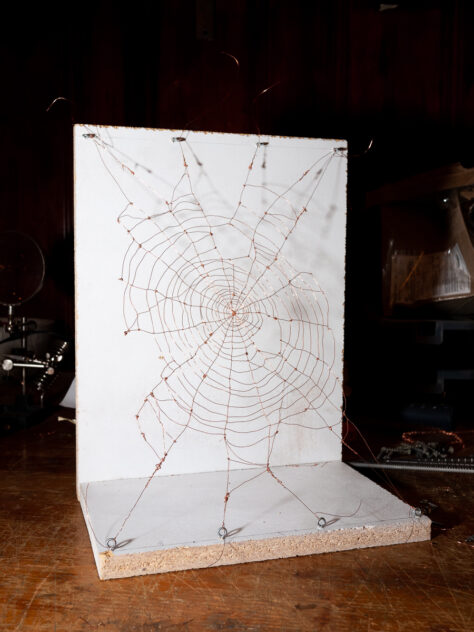 UUUUUU by Bradly Brown — process shot of a hand-formed copper-wire spiderweb stretched across a white panel in the studio