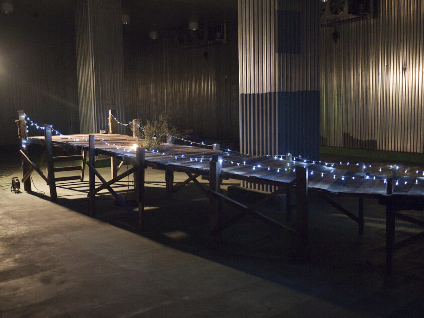 Damemoto (Nothing to Lose), 2012 — artwork by artist Bradly Brown. Low wooden pier stretching across the gallery floor in Hiroshima, edged with string lights