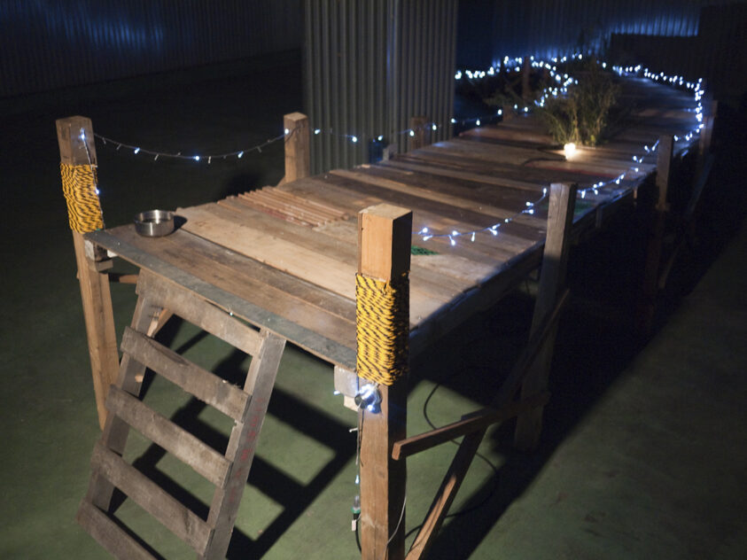 Damemoto (Nothing to Lose), 2012 — artwork by artist Bradly Brown. End of a wooden pier with a ladder, edged in blinking blue string lights