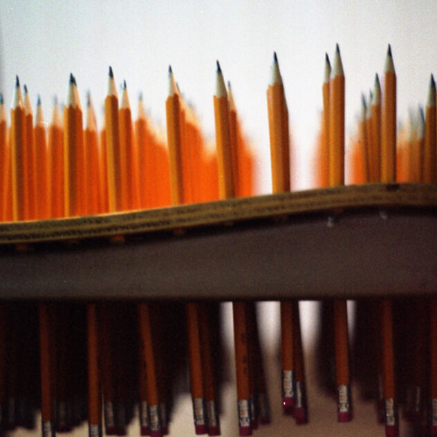 15,540 Miles, 2002 — artwork by artist Bradly Brown. Close-up of yellow No. 2 pencils rising from a school desk