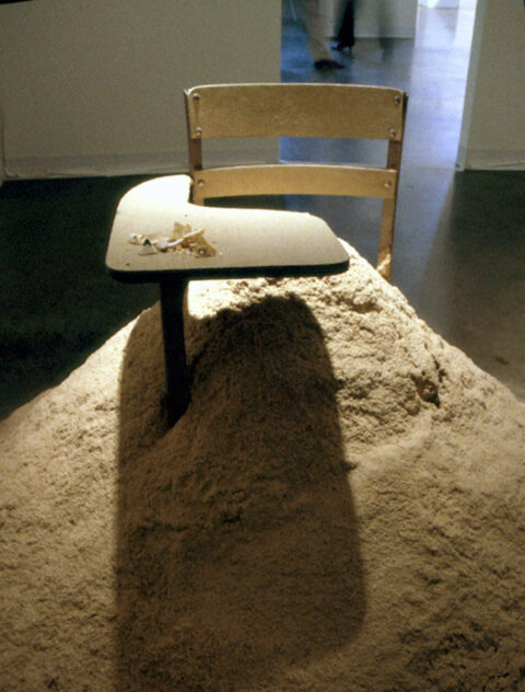 15,540 Miles, 2002 — artwork by artist Bradly Brown. School desk buried in a mound of sawdust and pencil shavings